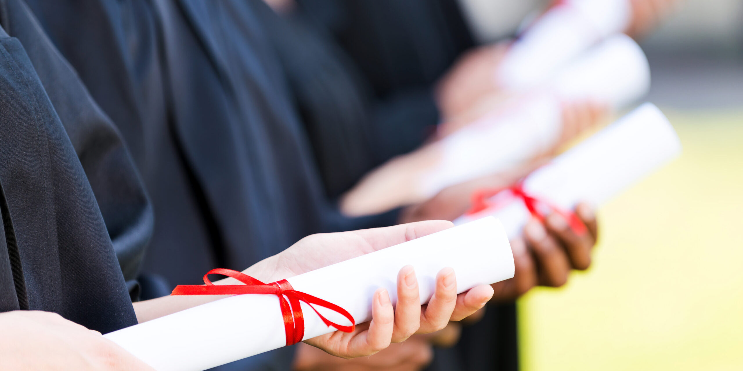 Graduates with diplomas. Close-up of four college graduates standing in a row and holding their diplomas